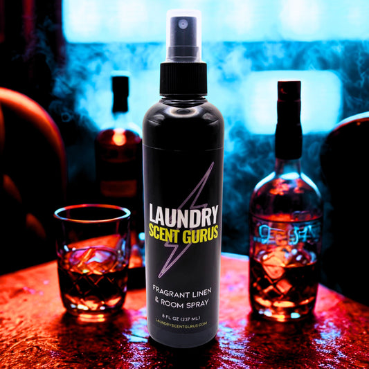 Laundry Scent Gurus spray bottle on a table with drinks and a blue light in the background