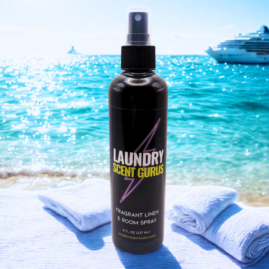 Bottle of Laundry Scent Gurus spray on a towel with a beach and boat in the background