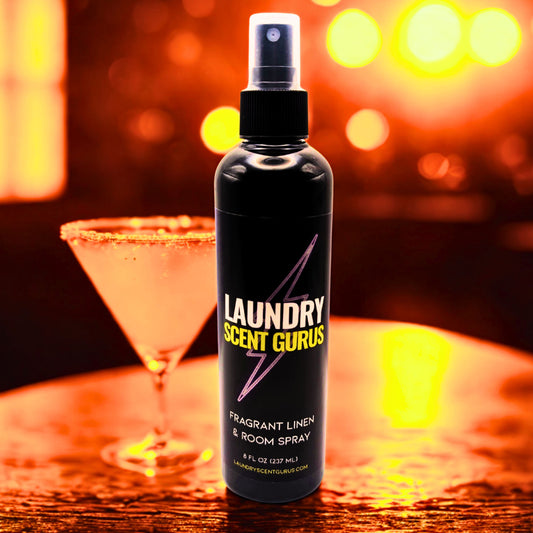 Bottle of Laundry Scent Gurus spray on a bar with a cocktail in the background